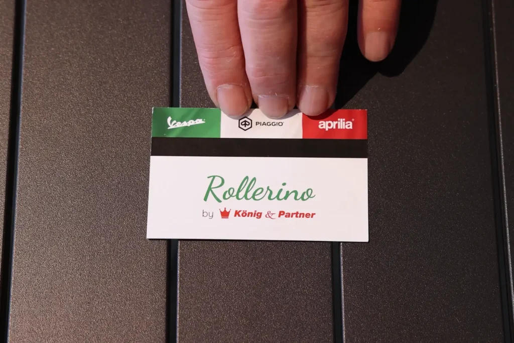 Ausschnitt Videowerbung Rollerino: Nahaufnahme Hand schiebt Visitenkarte über Tisch